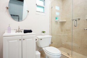 A bathroom with a toilet, sink, mirror, and shower.