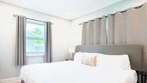 Quarto de hotel com cama, cortinas, janela e mesa de cabeceira.
