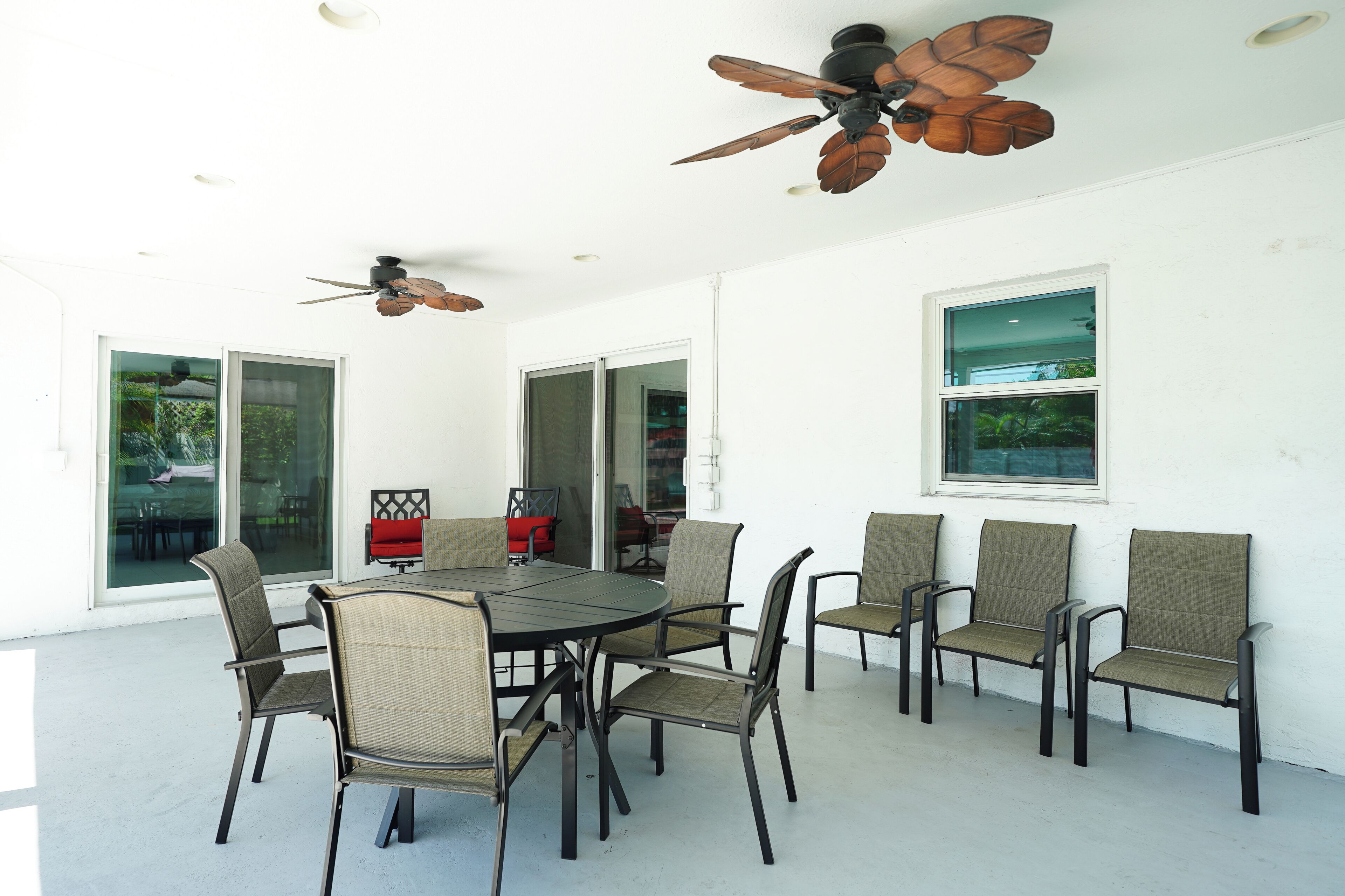 A dining area with a round table, six chairs, ceiling fans, and large windows.