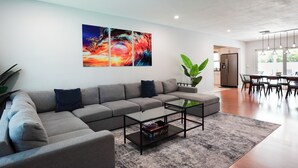 Uma sala de estar moderna com um sofá seccional, uma mesa de centro de vidro e uma grande pintura abstrata na parede.