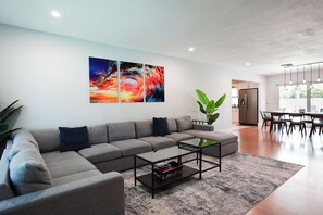 A modern living room with a sectional sofa, a glass coffee table, and a large abstract painting on the wall.