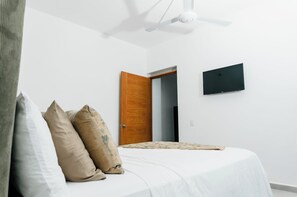 Ein Schlafzimmer mit einem Bett, Kissen, einem Deckenventilator, einer Tür und einem an der Wand befestigten Fernseher.