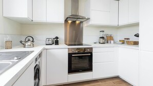 Een moderne keuken met witte kasten, een roestvrijstalen afzuigkap, een ingebouwde oven en een wasmachine.