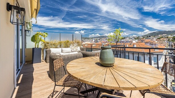 Een balkon met rieten meubels, een ronde houten tafel en een grote vaas.