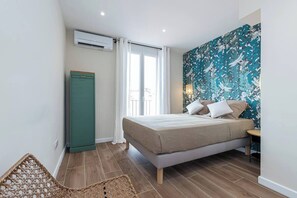 Ein Schlafzimmer mit Bett, Kleiderschrank, einem Fenster mit Vorhängen und einer Wand mit Blumenmuster.