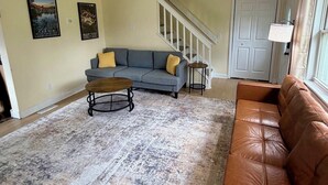 A living room with a gray sofa, a brown leather couch, a coffee table, and a patterned rug. There is a staircase leading to another level, a door, and two wall-mounted pictures. - Black Hills Gateway 

#CIMISC26-0010 (Rapid City)