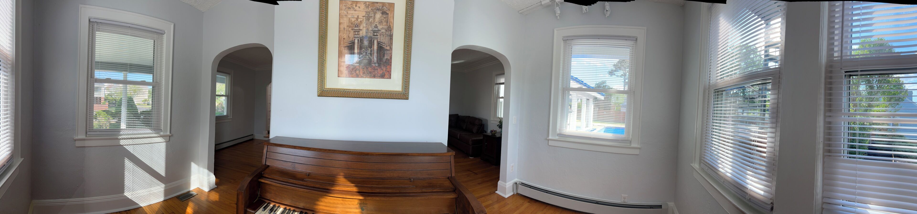 A hallway with wooden flooring, white walls, and multiple windows with blinds.