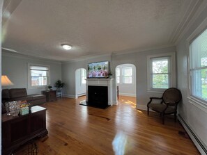 A spacious living room with hardwood floors, a fireplace, a television, and large windows. - Welcoming 3-bedroom house with AC in charming Norfolk (Norfolk)