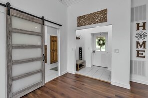 Un couloir avec une porte-fenêtre coulissante, un banc, un panneau d’accueil et un élément décoratif fixé au mur.