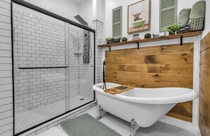 Une salle de bain dotée d’une douche à parois de verre, d’une baignoire sur pieds et d’une tête de lit en bois.