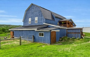 A large blue barn with a sloped roof, a wooden porch, and a fenced yard.
