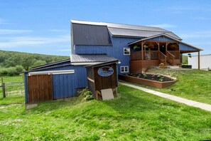 A two-story blue house with a wooden porch, a garage, and a garden.