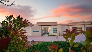 A modern building with a central entrance, surrounded by greenery and a sunset sky. - 4BR Luxury Retreat | Red Rock & Golf Course Views + Sauna, Geo Dome & Yoga (Sedona)