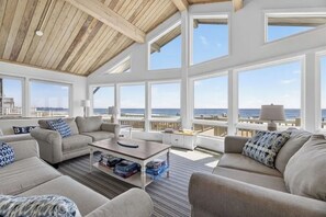A spacious living room with large windows, a high ceiling, and a view of the ocean.
