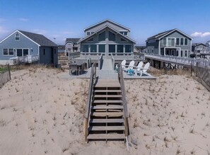 A beachfront property with a wooden boardwalk leading to a large house with multiple decks and outdoor seating.