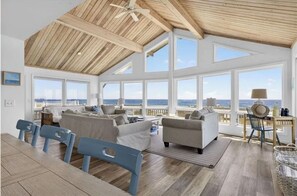 A spacious living area with a high ceiling, large windows, and a view of the ocean.
