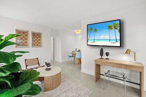 Ein modernes Wohnzimmer mit rundem Couchtisch, einem an der Wand montierten Fernseher, einem Holztisch und einem Essbereich mit Stühlen.