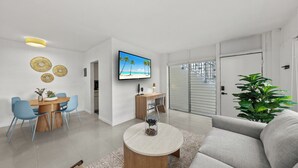 Uma sala de estar moderna com área de jantar, televisão de tela plana e uma planta grande.