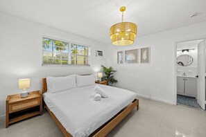 Ein Schlafzimmer mit Bett, Nachttisch, Lampe, Fenster und Blick nach draußen.