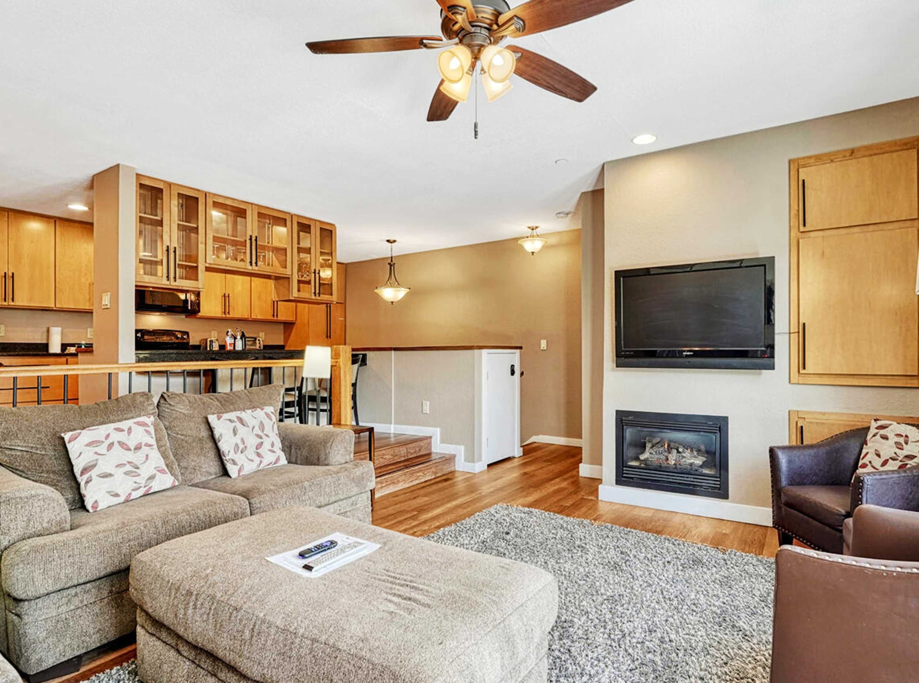 A modern living room with a sofa, ottoman, fireplace, TV, and wooden cabinets.