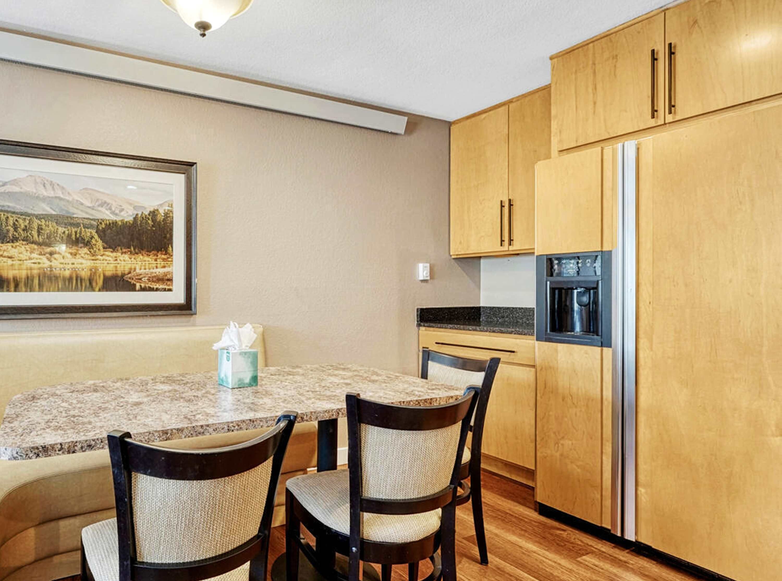 A dining area with a table, chairs, a framed picture, and wooden cabinets.