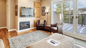 A living room with a fireplace, a television, a sofa, and a balcony with a view. - Crestview Place Mountain View, Balcony & Shuttle (Winter Park)