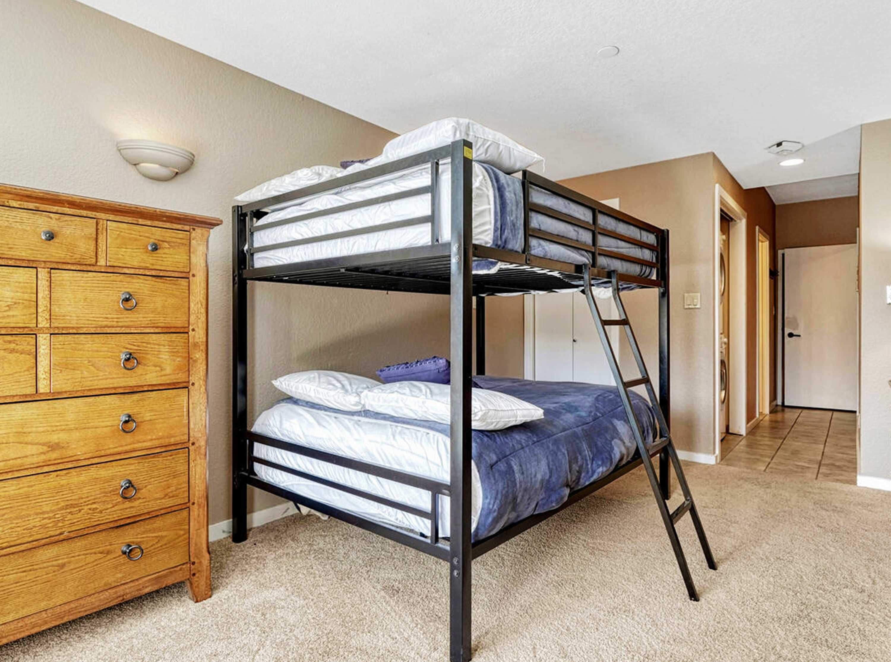 A bunk bed with a ladder, a wooden dresser with drawers, and a hallway leading to a door.