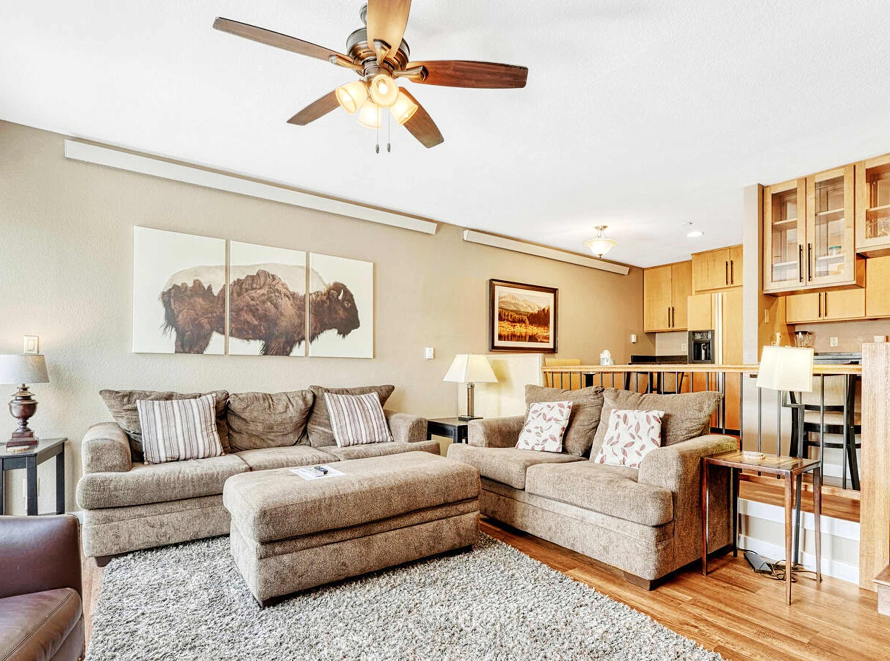 A living room with a sofa set, a ceiling fan, and artwork on the wall.