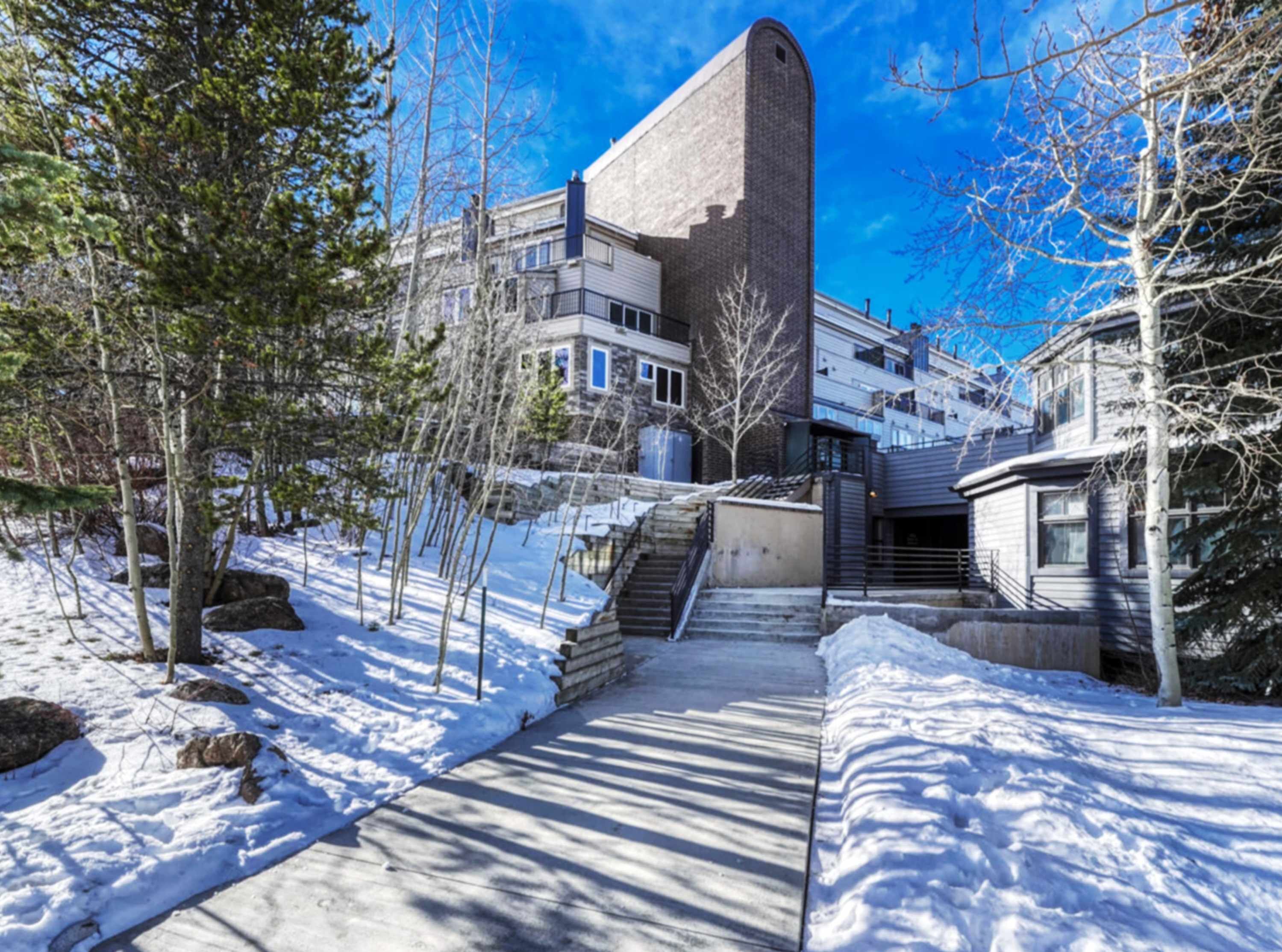 A building with a unique architectural design, a snow-covered pathway, and surrounding trees.