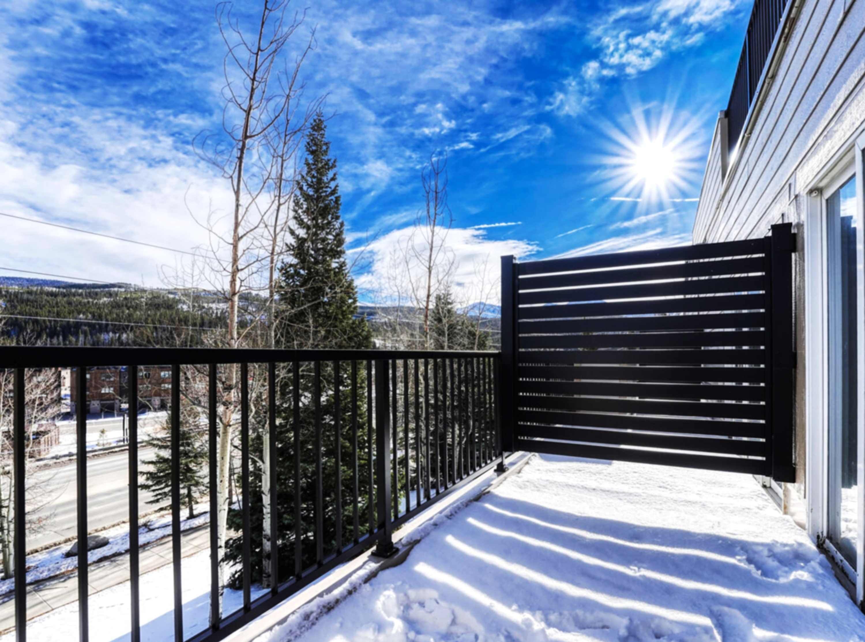 Een sneeuwbedekt balkon met een zwarte reling, een heldere lucht en een berg op de achtergrond.