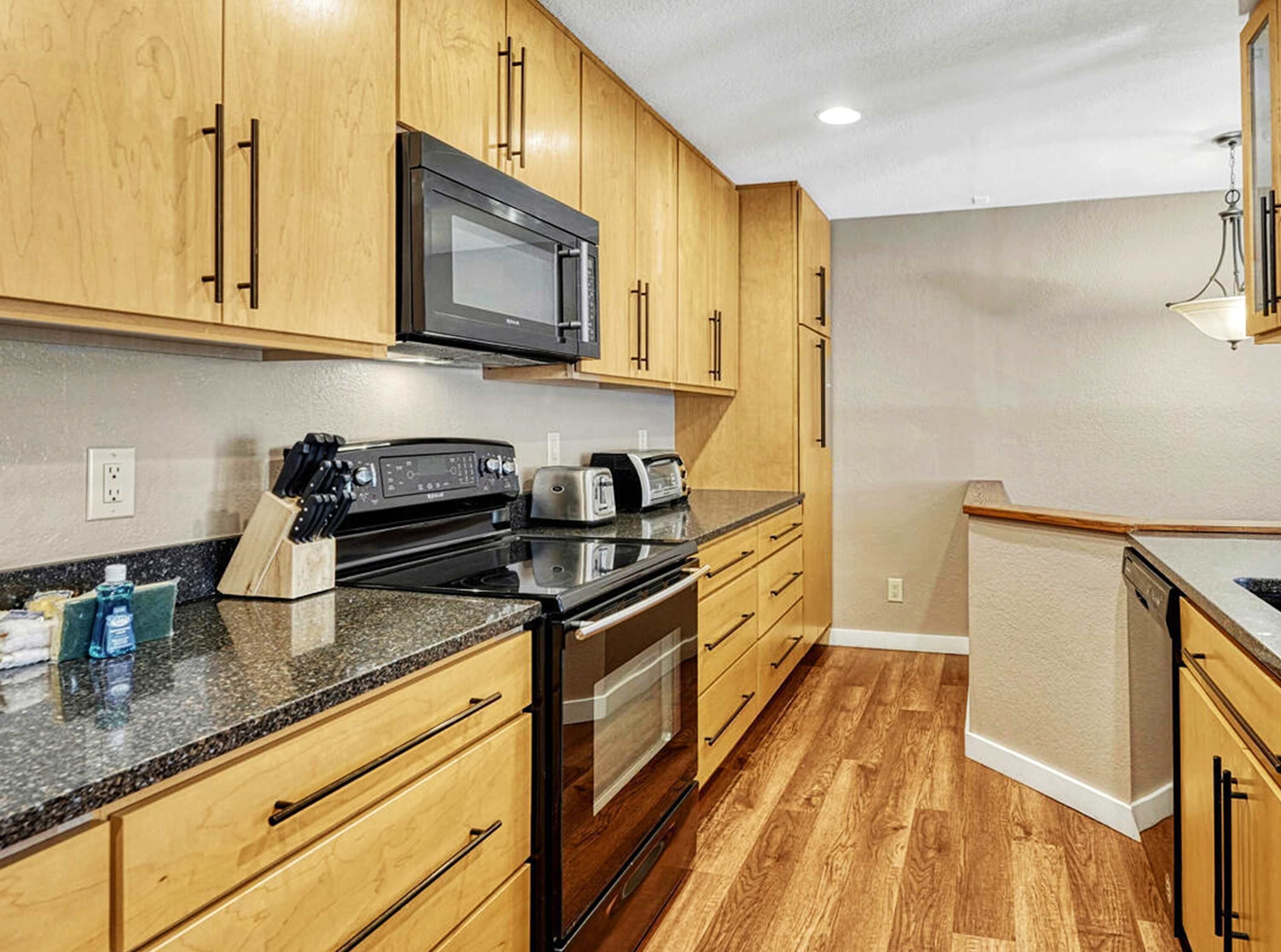 Une cuisine avec des meubles de rangement en bois, un four à micro-ondes, un grille-pain et une cuisinière.