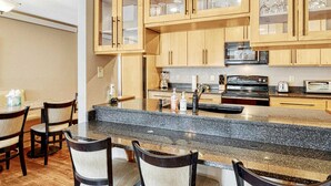 A kitchen with wooden cabinets, a granite countertop, and a dining area with chairs. - Crestview Place Mountain View, Balcony & Shuttle (Winter Park)