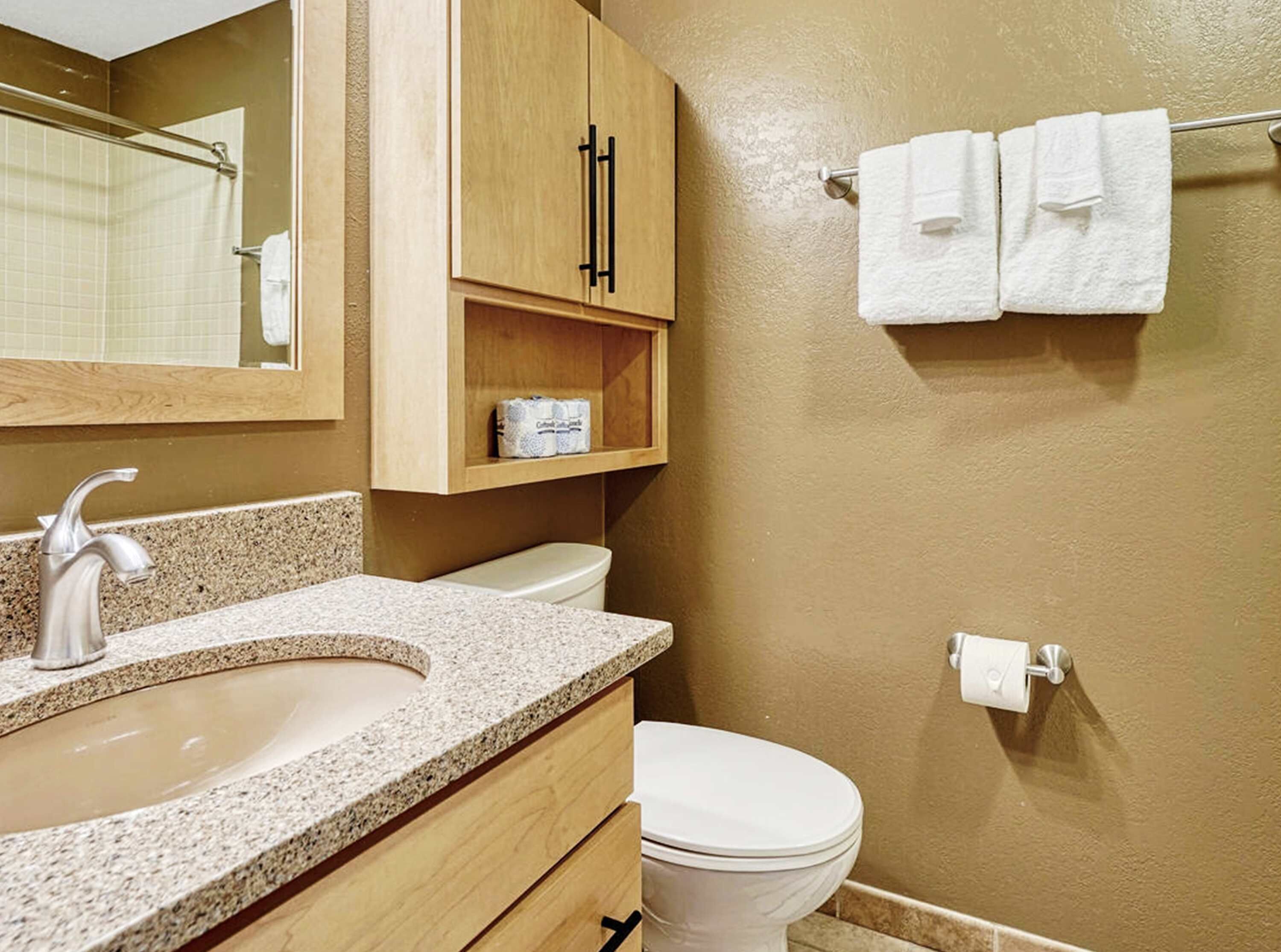 Een badkamer met een wastafel met granieten blad, een toilet, een houten kast en een handdoekrek met handdoeken.