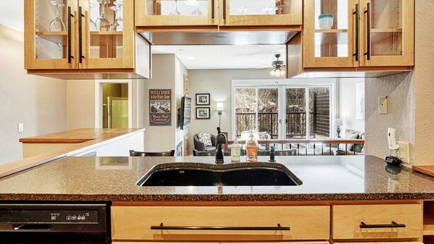 A kitchen with wooden cabinets, a granite countertop, a dishwasher, and a view to the living area. - Crestview Place Mountain View, Balcony & Shuttle (Winter Park)