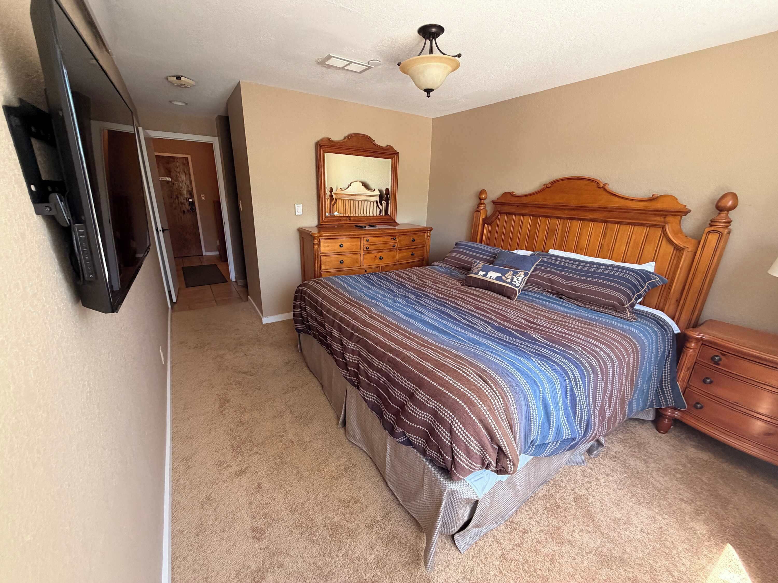 A bedroom with a bed, dresser, mirror, and TV.