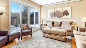 A spacious living room with a ceiling fan, a large sliding glass door leading to a balcony, and a mounted artwork of bison. - Crestview Place Mountain View, Balcony & Shuttle (Winter Park)