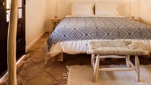 A bedroom with a bed, two bedside lamps, a wooden bench, a woven chair, and a rustic door. - CASA RIBA - between ocean & countryside with pool (caparica)