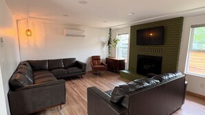 A modern living room with a sectional sofa, a fireplace, and a television mounted on a brick wall. - Cozy 2-bedroom house in tranquil Prescott Valley with AC (Prescott Valley)