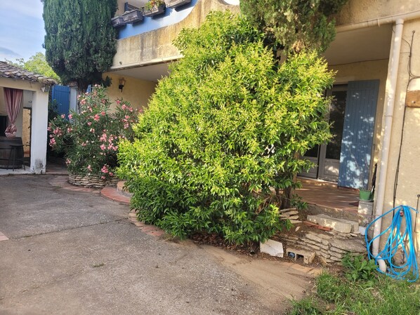 A house with a paved driveway, a stone wall, and a large bush with pink flowers. - Summer rental Avignon festival House 100m2. Perfect for relaxing. (Avignon)