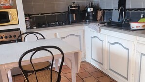 Eine Küche mit weißem Tisch, Stühlen, einem Herd, einer Mikrowelle, einer Kaffeemaschine und einem Spülbecken.