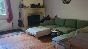 Ein Wohnzimmer mit Kamin, einem grünen Sofa, Fliesenboden und einem Holztisch.