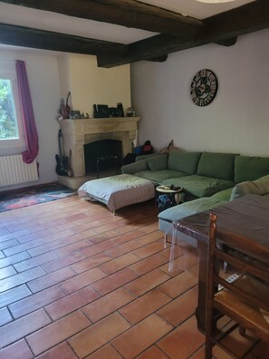 Ein Wohnzimmer mit Kamin, einem grünen Sofa, Fliesenboden und einem Holztisch.