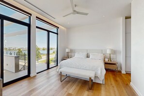 A modern bedroom with a large window, a bed, a bench, and a ceiling fan. - 7 Bedroom Waterfront Rehoboth beach house with private pool (Rehoboth Beach)