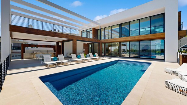 Ein moderner Poolbereich mit Liegestühlen, einem klaren, blauen Pool und einem zeitgemäßen Gebäude mit großen Fenstern.