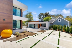 Ein modernes, zweistöckiges Haus mit Garage, einer gepflasterten Auffahrt mit Grasstreifen und einem großen, gelben Zierteil.