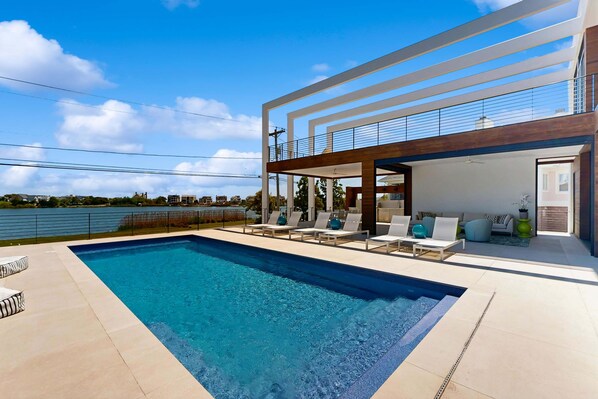 A modern house with a swimming pool, outdoor seating, and a view of the water. - 7 Bedroom Waterfront Rehoboth beach house with private pool (Rehoboth Beach)