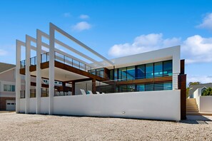 A modern building with a flat roof, large windows, and a gravel driveway. - 7 Bedroom Waterfront Rehoboth beach house with private pool (Rehoboth Beach)