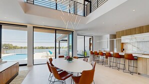 Eine moderne Küche mit Marmorarbeitsplatte, ein Essbereich mit rundem Tisch und Stühlen sowie Blick auf einen Pool.