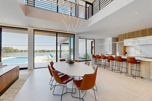 Eine moderne Küche mit Marmorarbeitsplatte, ein Essbereich mit rundem Tisch und Stühlen sowie Blick auf einen Pool.