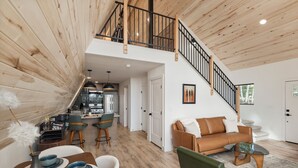 A spacious loft-style living area with a kitchen, dining table, and a staircase leading to an upper level. - Brand New A-Frame! Panoramic Mt Views, Hot Tub, Speakeasy, EV Charger (Florissant)